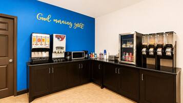 A kitchen area with a coffee station, a microwave, and a beverage dispenser.