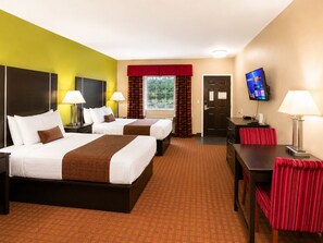 A hotel room with two beds, a desk, a TV, and a window with curtains. - Rodeway Inn Dilley I-35 (Dilley)