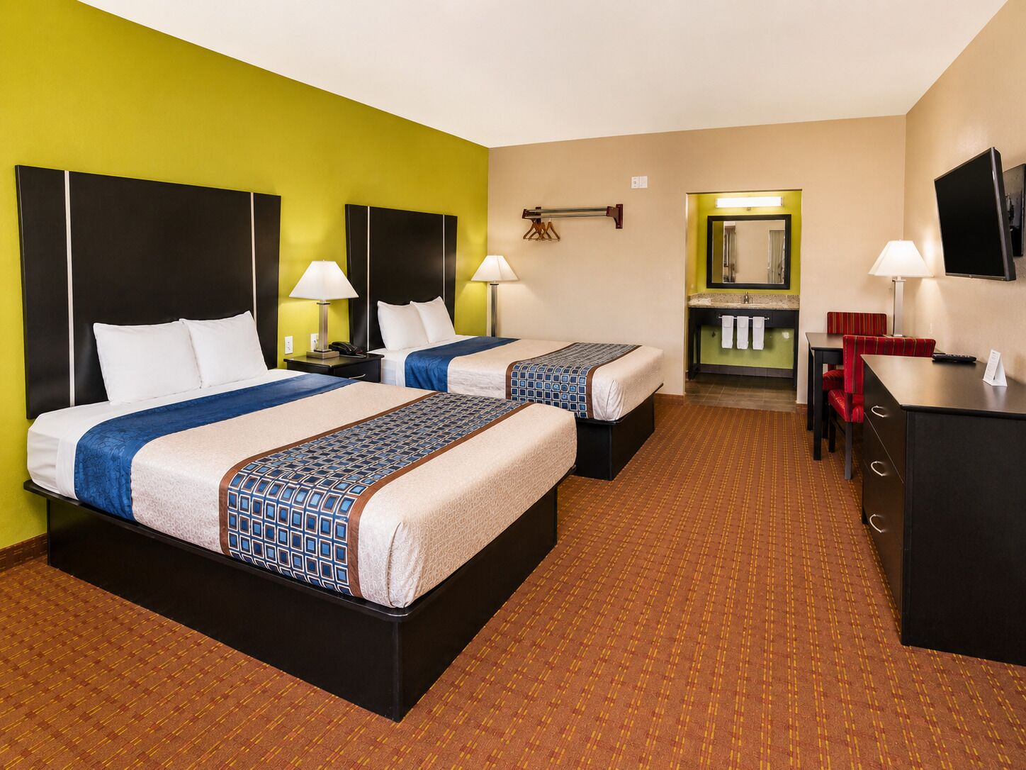 A hotel room with two beds, a desk, a chair, a TV, and a bathroom visible through an open door.