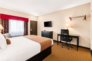 A hotel room with a bed, a desk, a chair, a television, and a window with curtains.