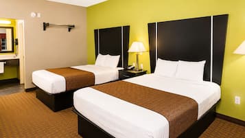 A hotel room with two beds, a nightstand with a lamp, a telephone, and a mirror on the wall.
