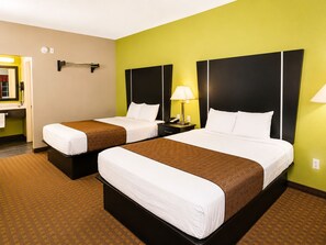 A hotel room with two beds, a nightstand with a lamp, a telephone, and a mirror on the wall. - Rodeway Inn Dilley I-35 (Dilley)