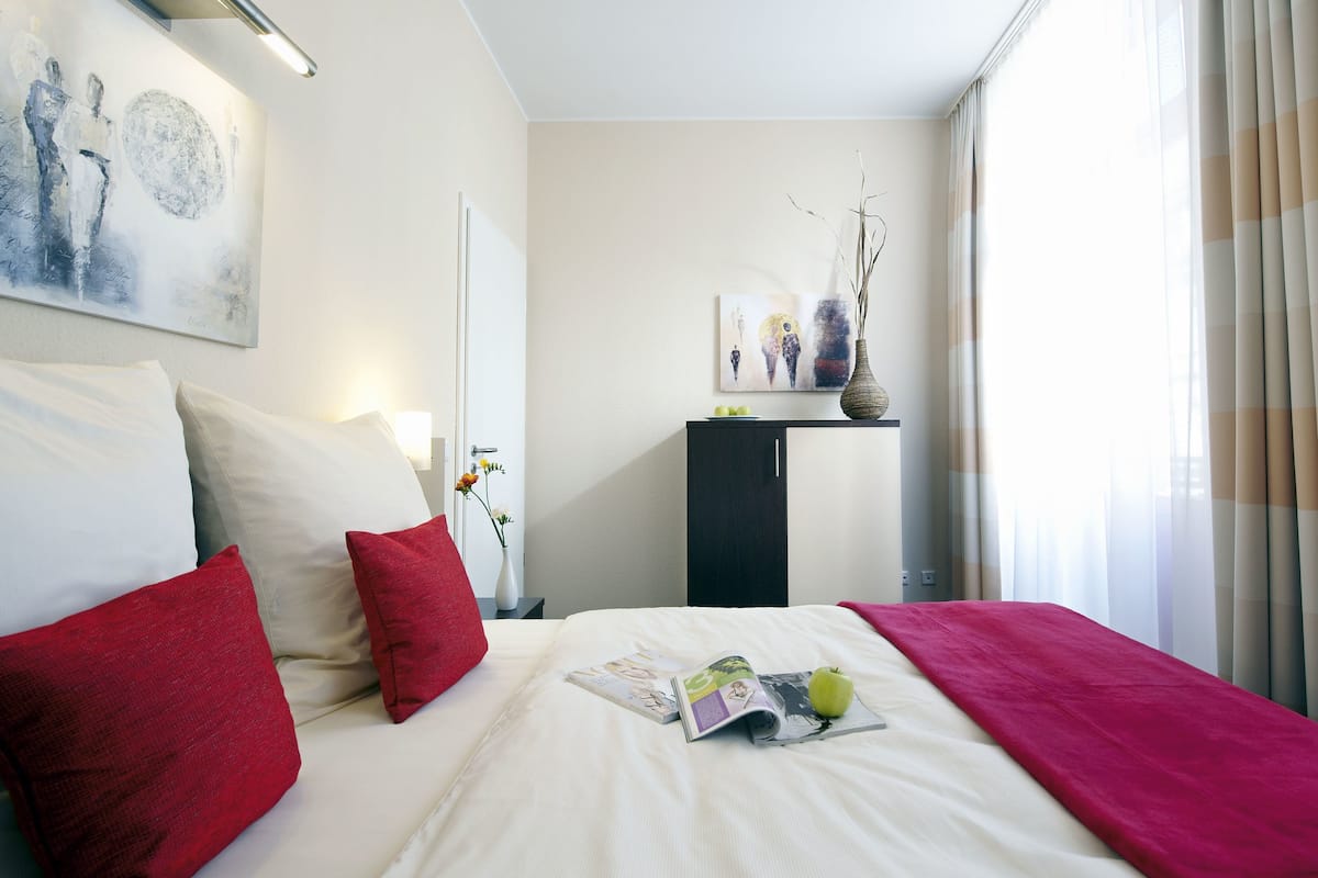 Una cama bien hecha con almohadas rojas y blancas, una revista y una manzana sobre la cama.