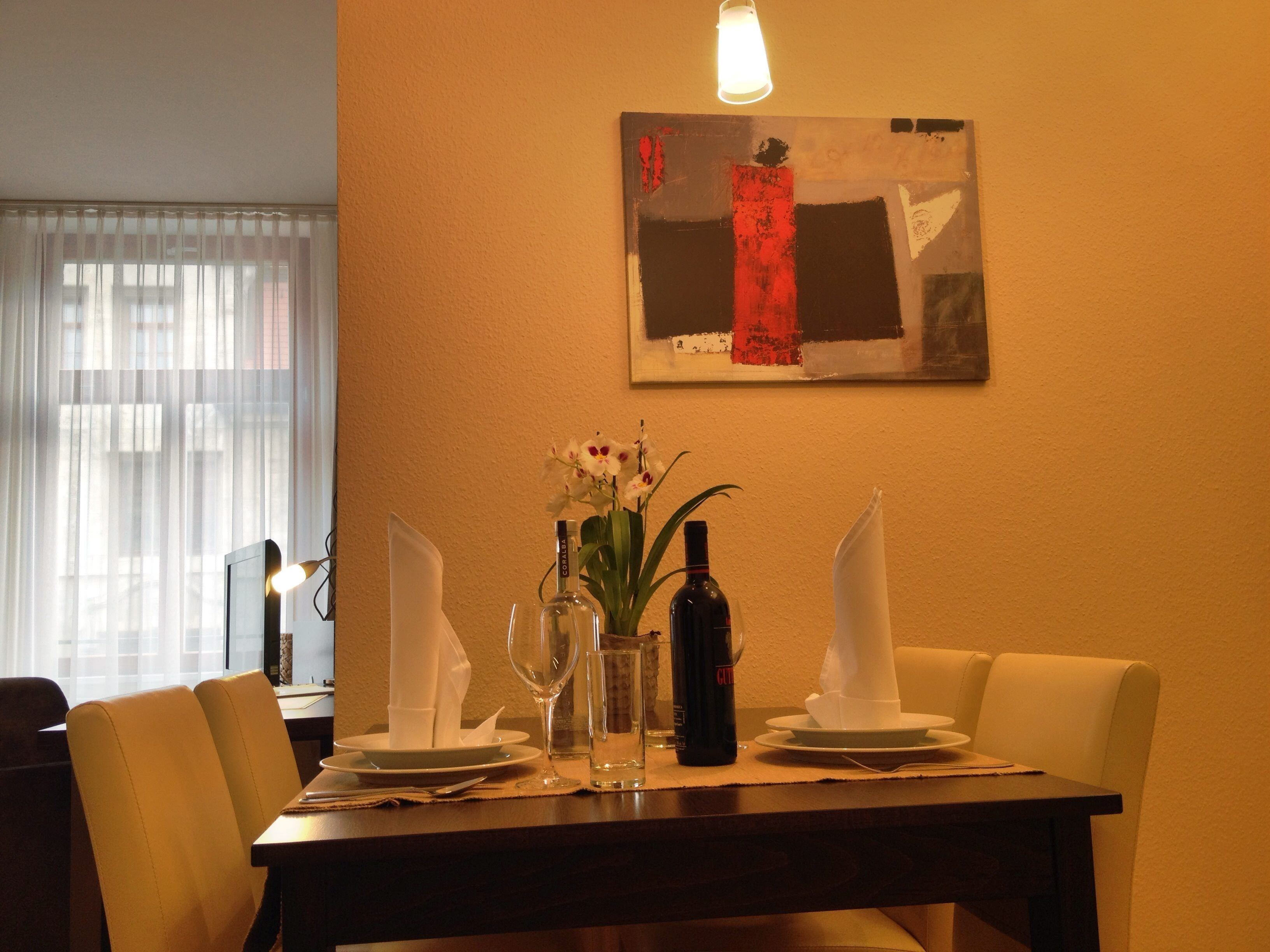 A dining table set with plates, a bottle, a vase with flowers, and a napkin holder.