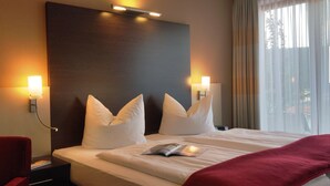 Une chambre d’hôtel avec un grand lit, deux lampes de chevet, une table de nuit, un fauteuil rouge et une fenêtre avec des rideaux.