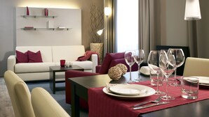 Une chambre d’hôtel moderne avec un coin repas, un canapé et une table dressée pour deux personnes.