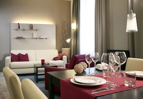 Una habitación de hotel moderna con zona de comedor, sofá y mesa dispuesta para dos.