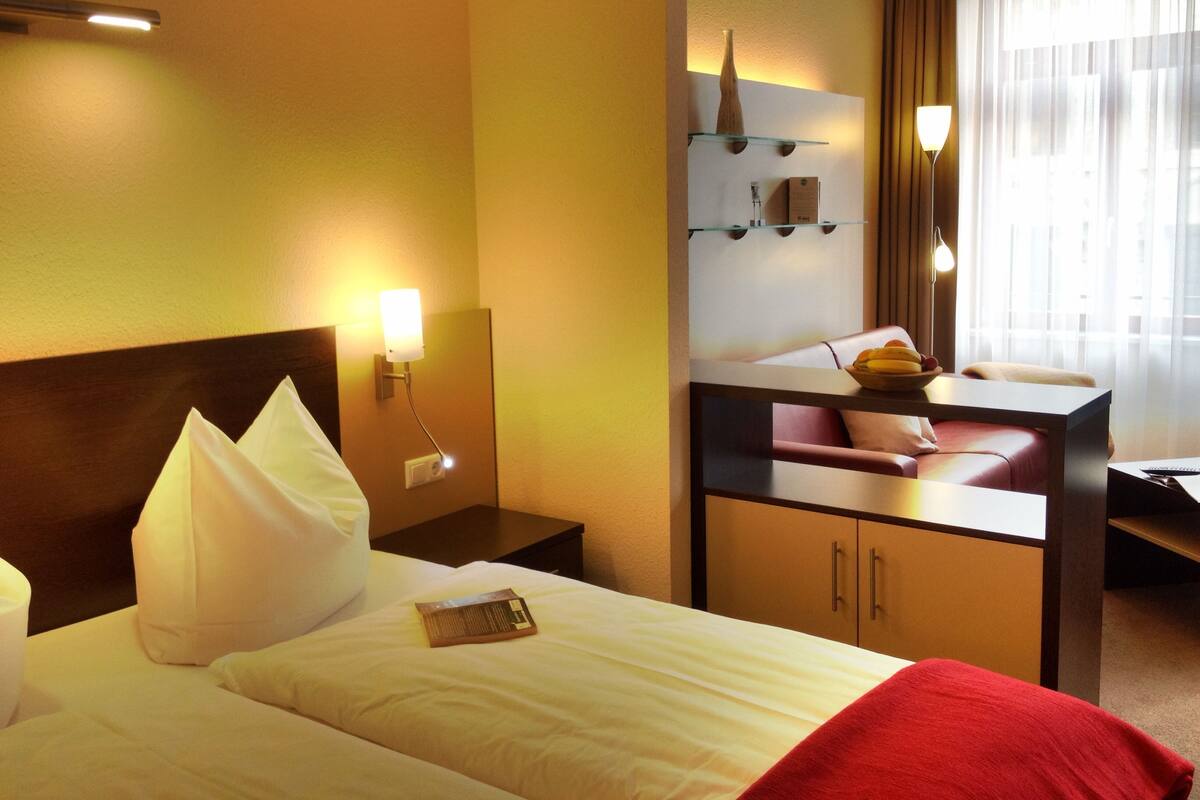Una habitación de hotel con una cama, un escritorio, una silla y una mesita con un frutero.