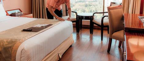 A hotel room with a large bed, a desk with a chair, and a view of the city through the window.