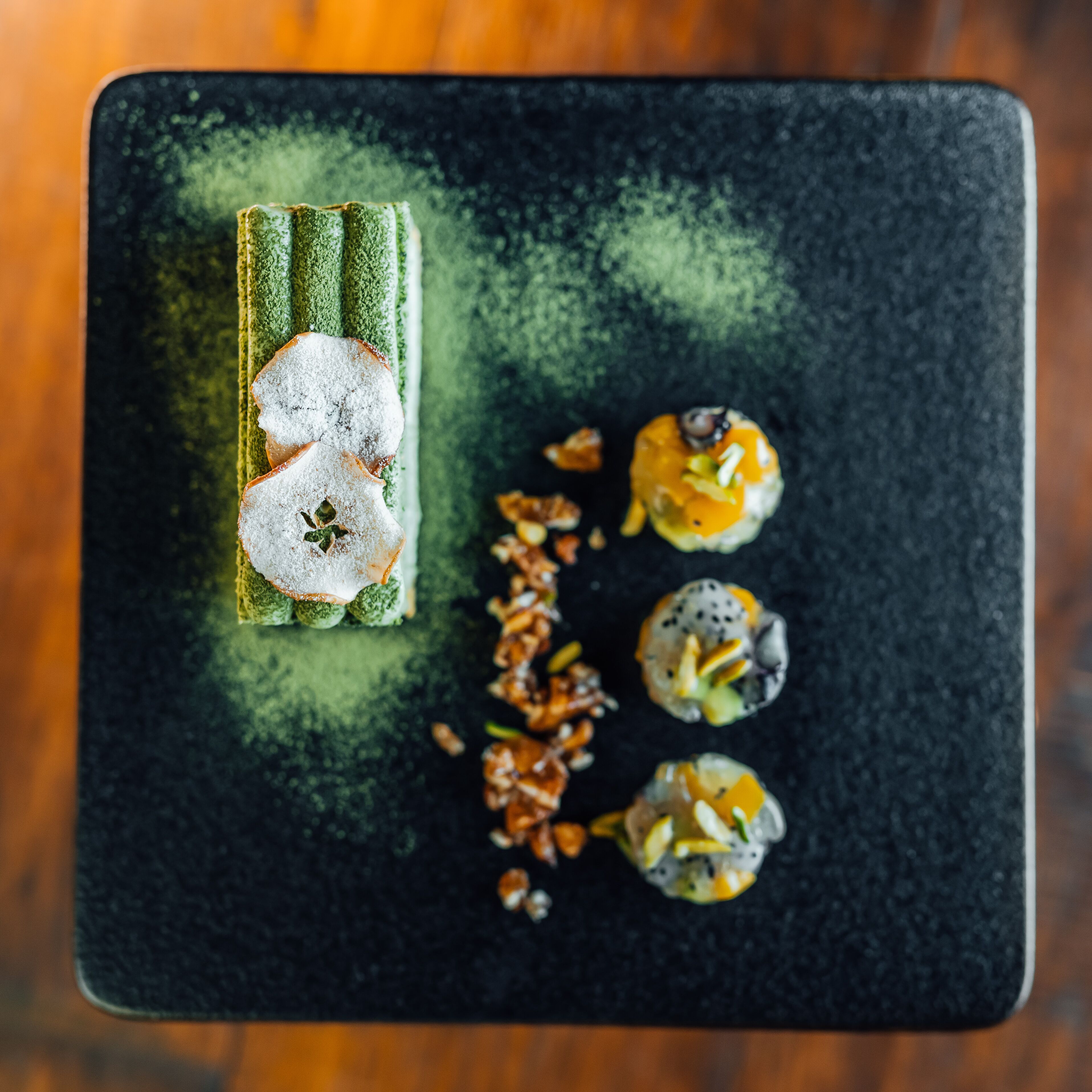Un plato cuadrado con fondo verde oscuro y una variedad de alimentos, incluyendo un pastel con forma de estrella y tres pequeñas reposterías con distintos ingredientes.