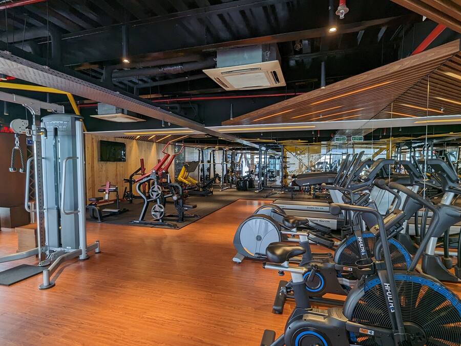 Un gimnasio con diversos equipos de ejercicio, incluyendo cintas de correr y máquinas de pesas, y suelo de madera.