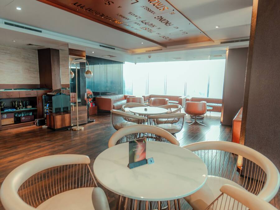 A modern interior with round tables and white chairs, a bar area, and a large window providing natural light.