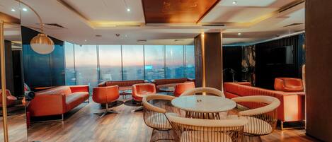 A modern lounge area with a city view, comfortable seating, and a wooden floor.
