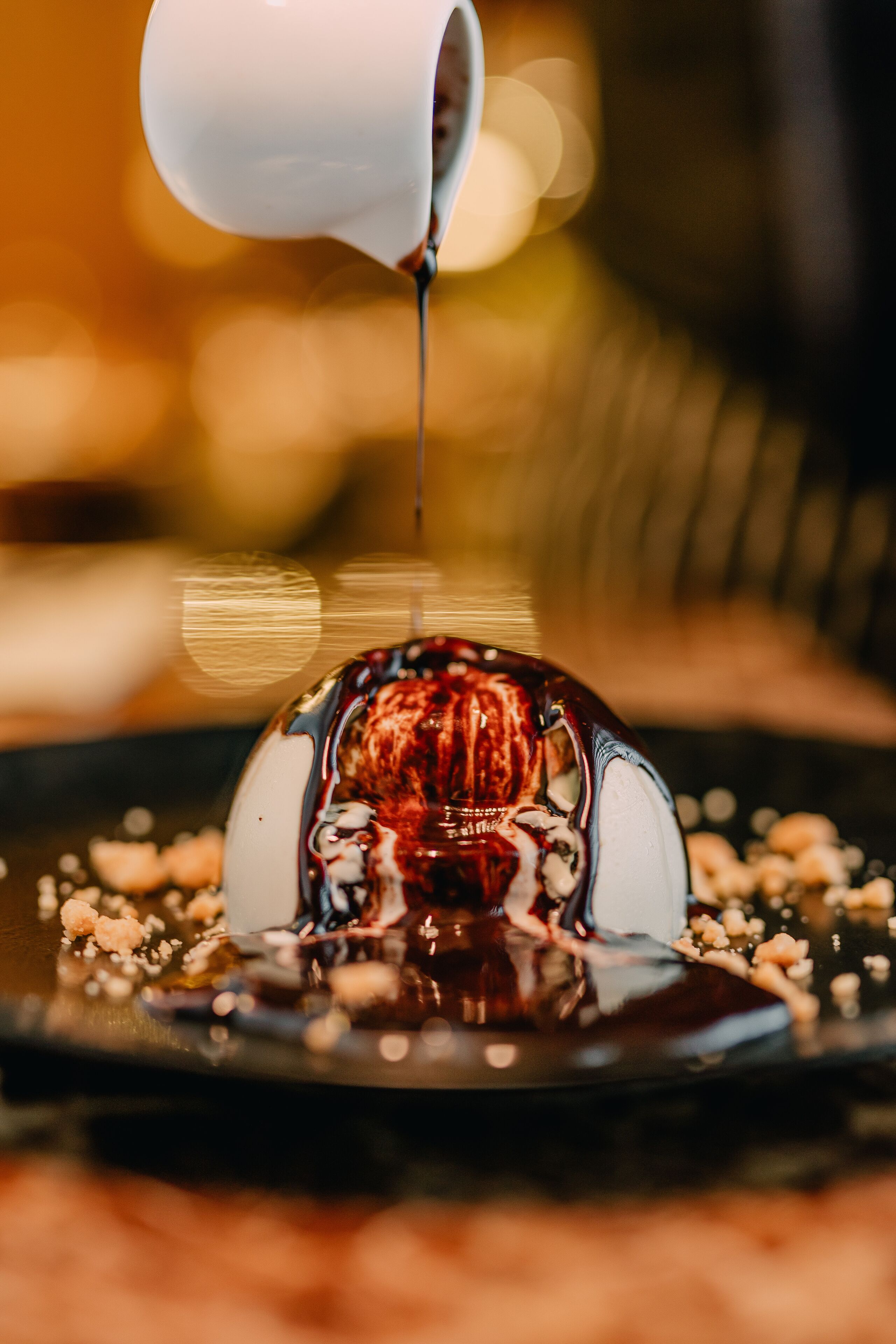 A dessert with a glossy topping, possibly chocolate, on a plate with scattered nuts.