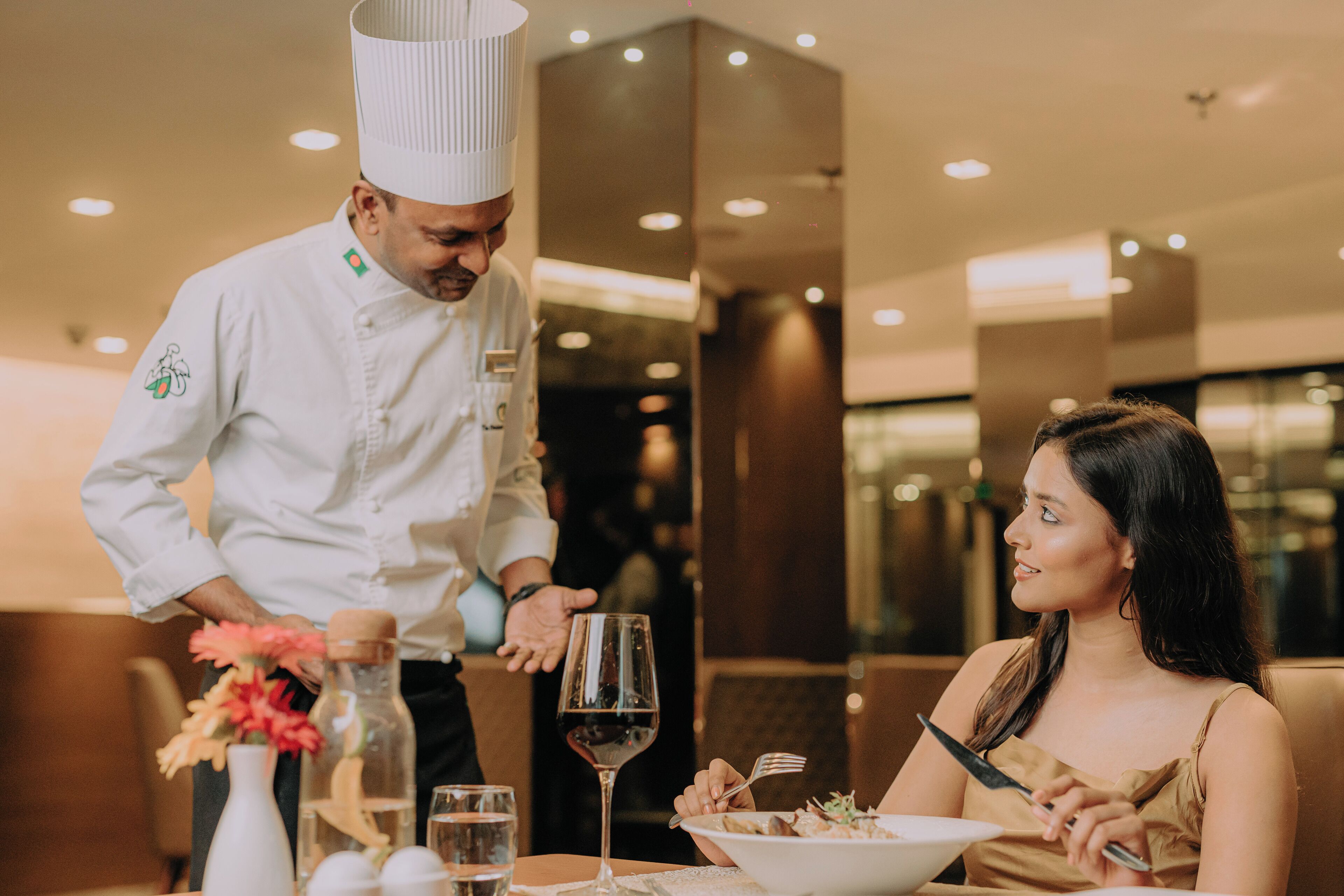 A restaurant interior with a chef serving a meal to a guest.