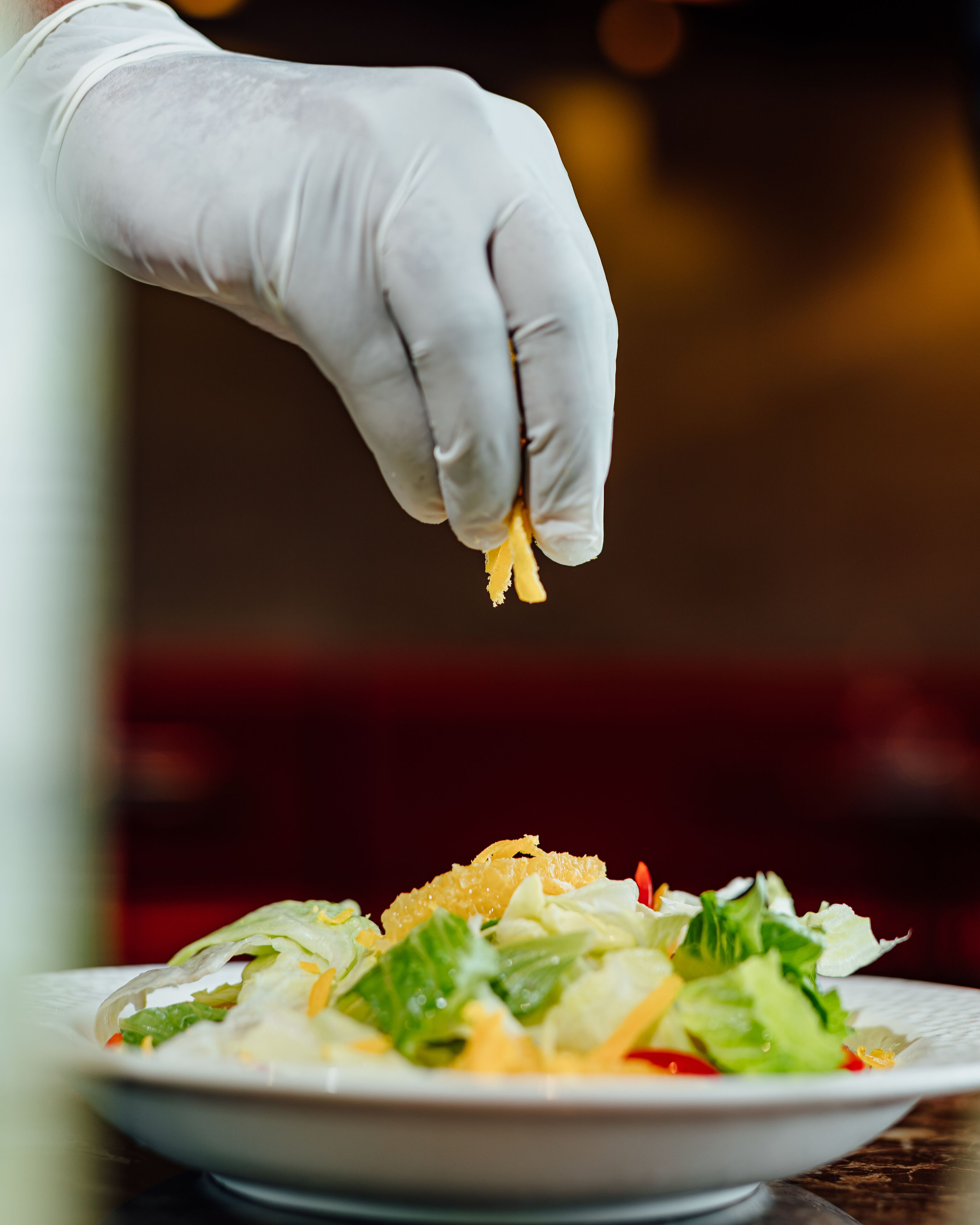 A hand wearing a white glove holding a piece of food over a plate of salad.