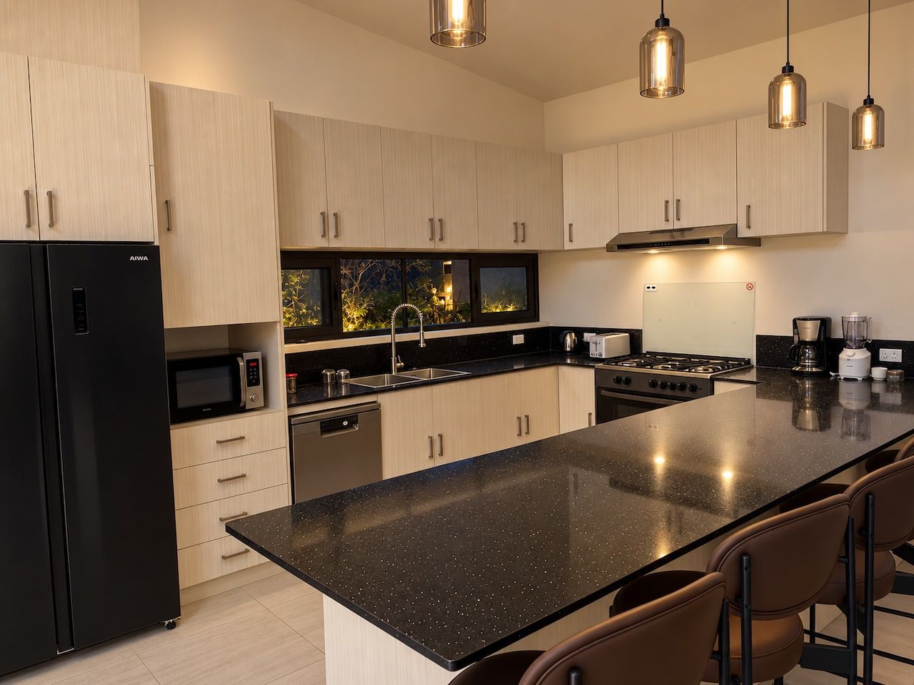 Una cocina moderna con una isla grande, electrodomésticos de acero inoxidable e iluminación colgante.