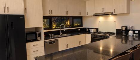Una cocina moderna con una isla grande, electrodomésticos de acero inoxidable e iluminación colgante.