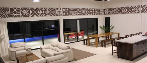 A spacious living area with a sofa set, a wooden coffee table, a dining table with chairs, and a kitchen island.