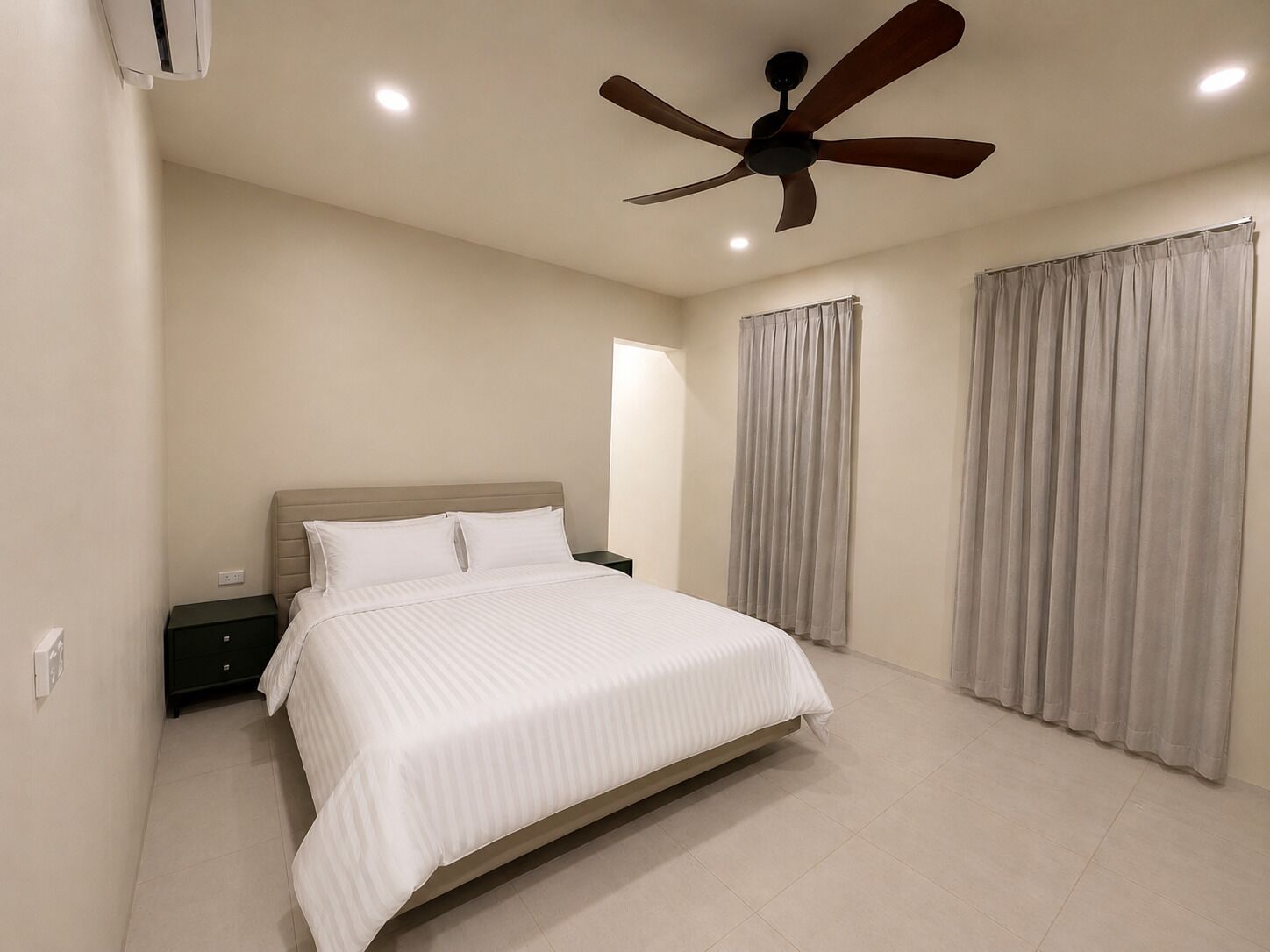 Un dormitorio con cama, ventilador de techo, mesita de noche y cortinas.