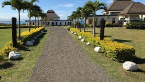 A pathway leading to a building with a tiled roof, surrounded by palm trees and yellow flowers. - Sapphire Bay Fiji (Lautoka)