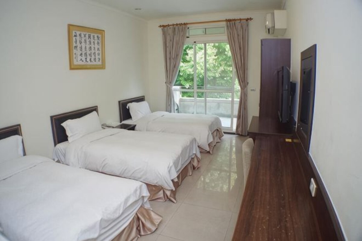 A hotel room with three beds, a television, and a balcony with curtains.