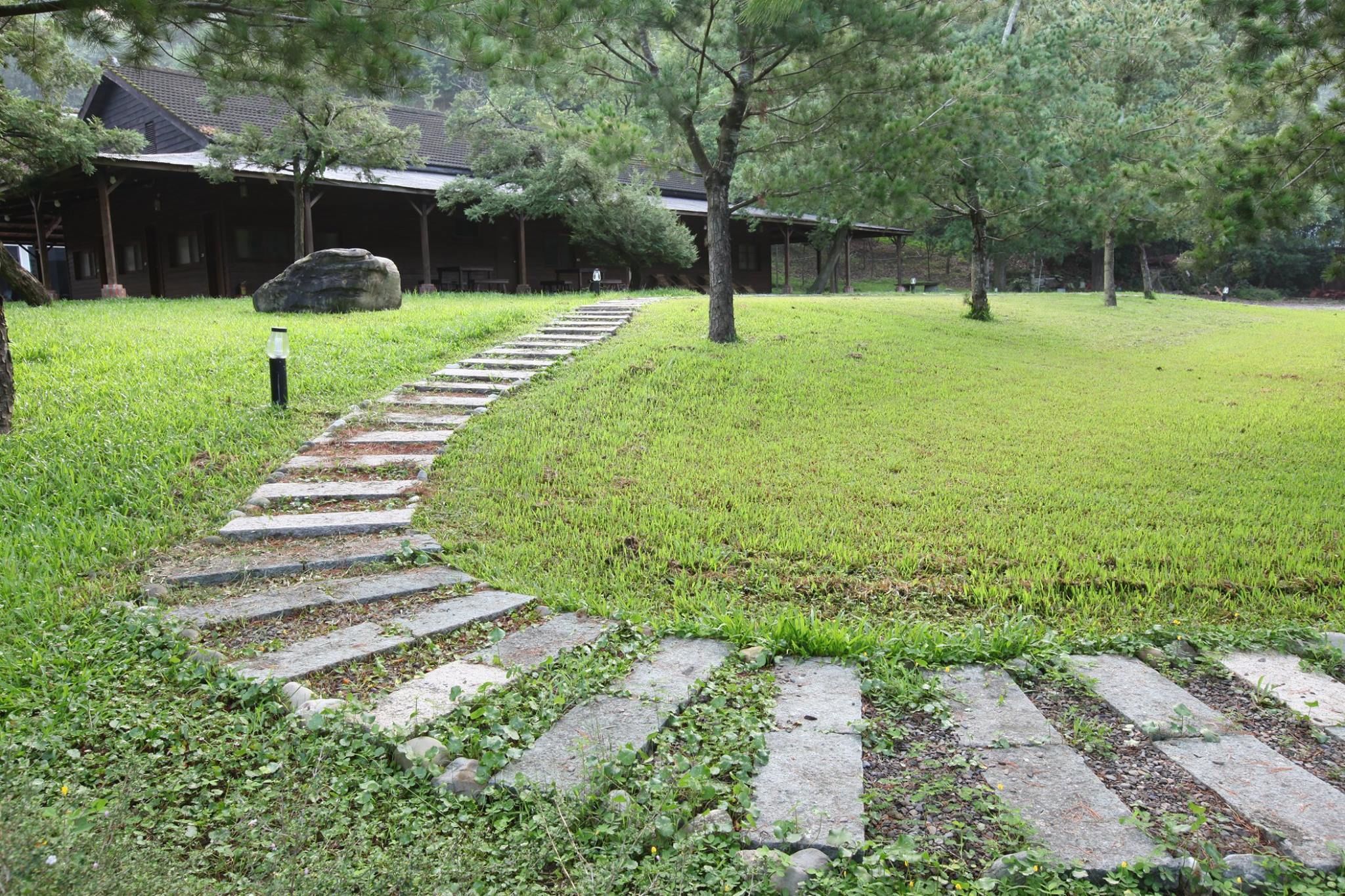 Un sentiero di pietra conduce a un edificio tradizionale circondato da erba e alberi.