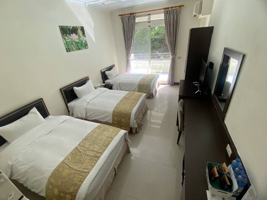 A hotel room with two beds, a desk, a television, and a window with curtains.