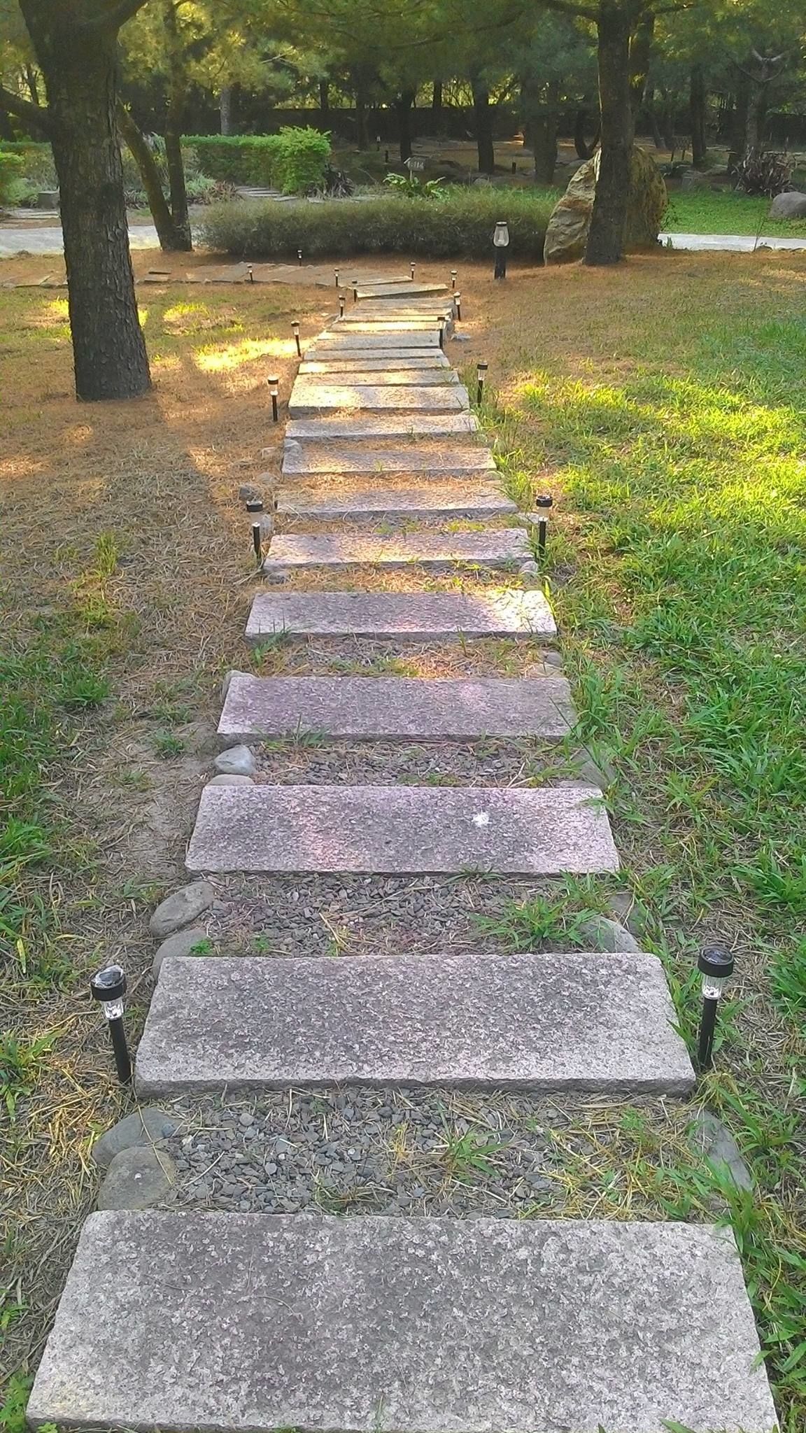 A stone pathway in a park with evenly spaced steps and lantern-style lights.