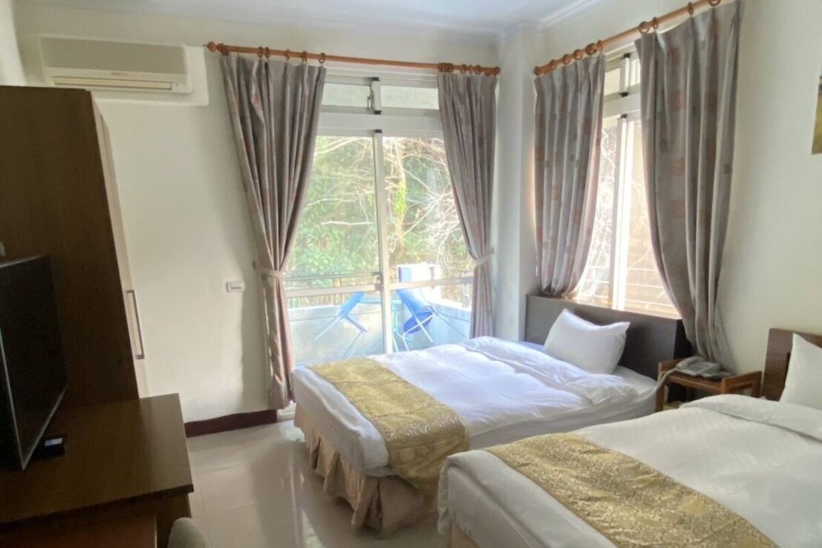 A hotel room with two beds, a desk, and a TV.