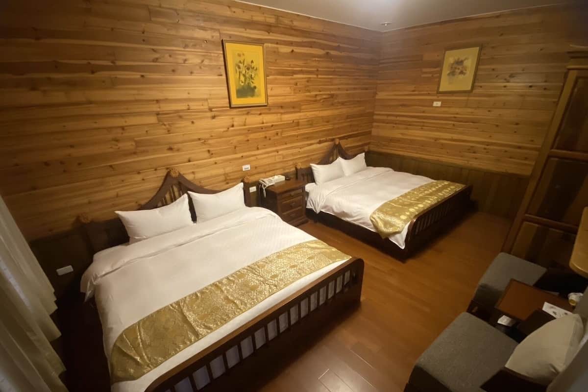 A room with two beds, wooden walls, and a small seating area.