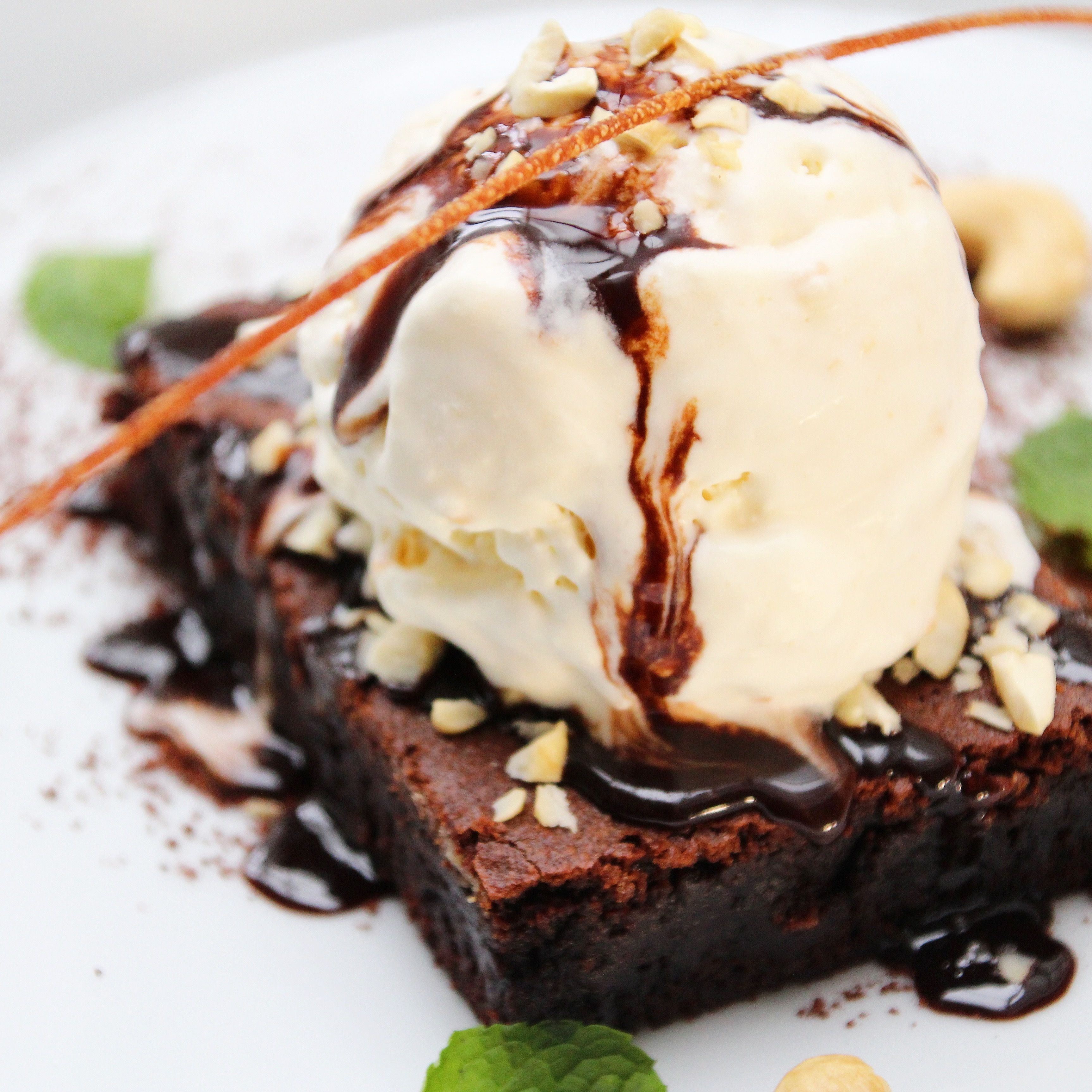 A dessert with ice cream, nuts, and chocolate sauce on a plate.