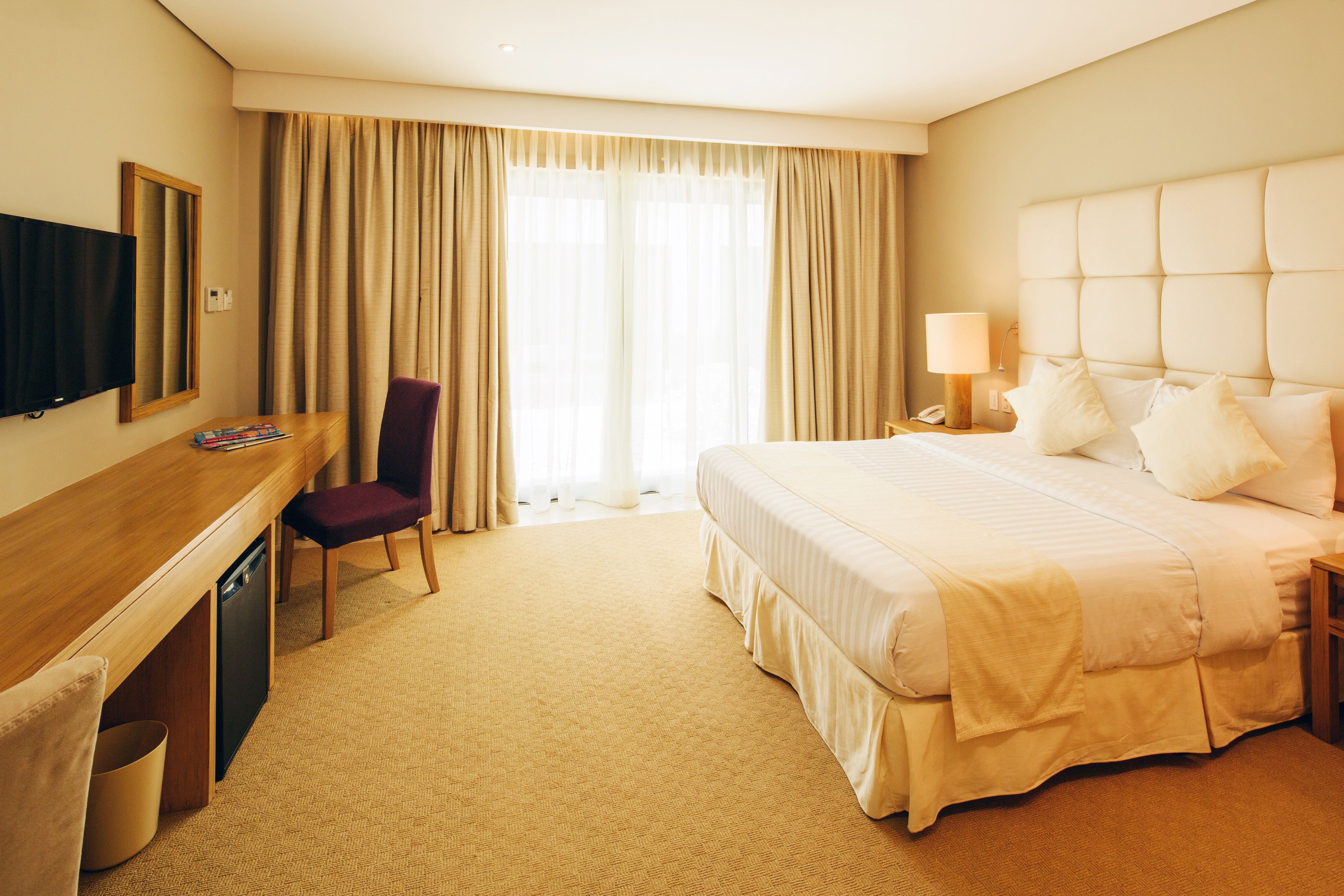 Una habitación de hotel con cama, escritorio, silla, televisor y ventana con cortinas.