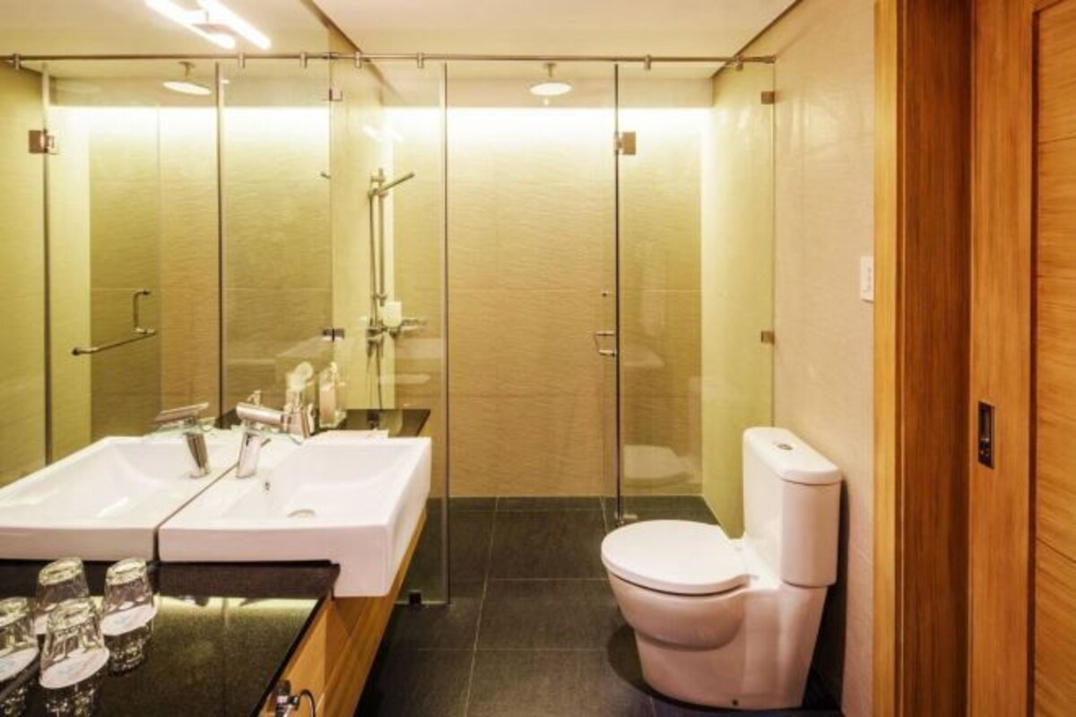 Un baño moderno con ducha de vidrio, lavamanos blanco con espejo y un inodoro.