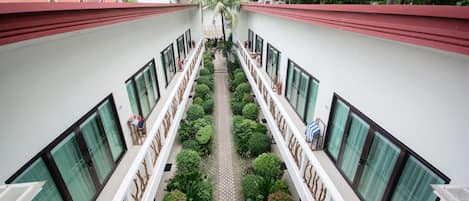Corredor de hotel com um caminho central ladeado por arbustos bem aparados e uma série de janelas de ambos os lados.