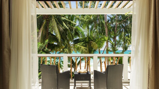 A sunlit outdoor seating area with wicker furniture and a view of palm trees and a beach. - Villa Caemilla Beach Boutique Hotel (Boracay Island)