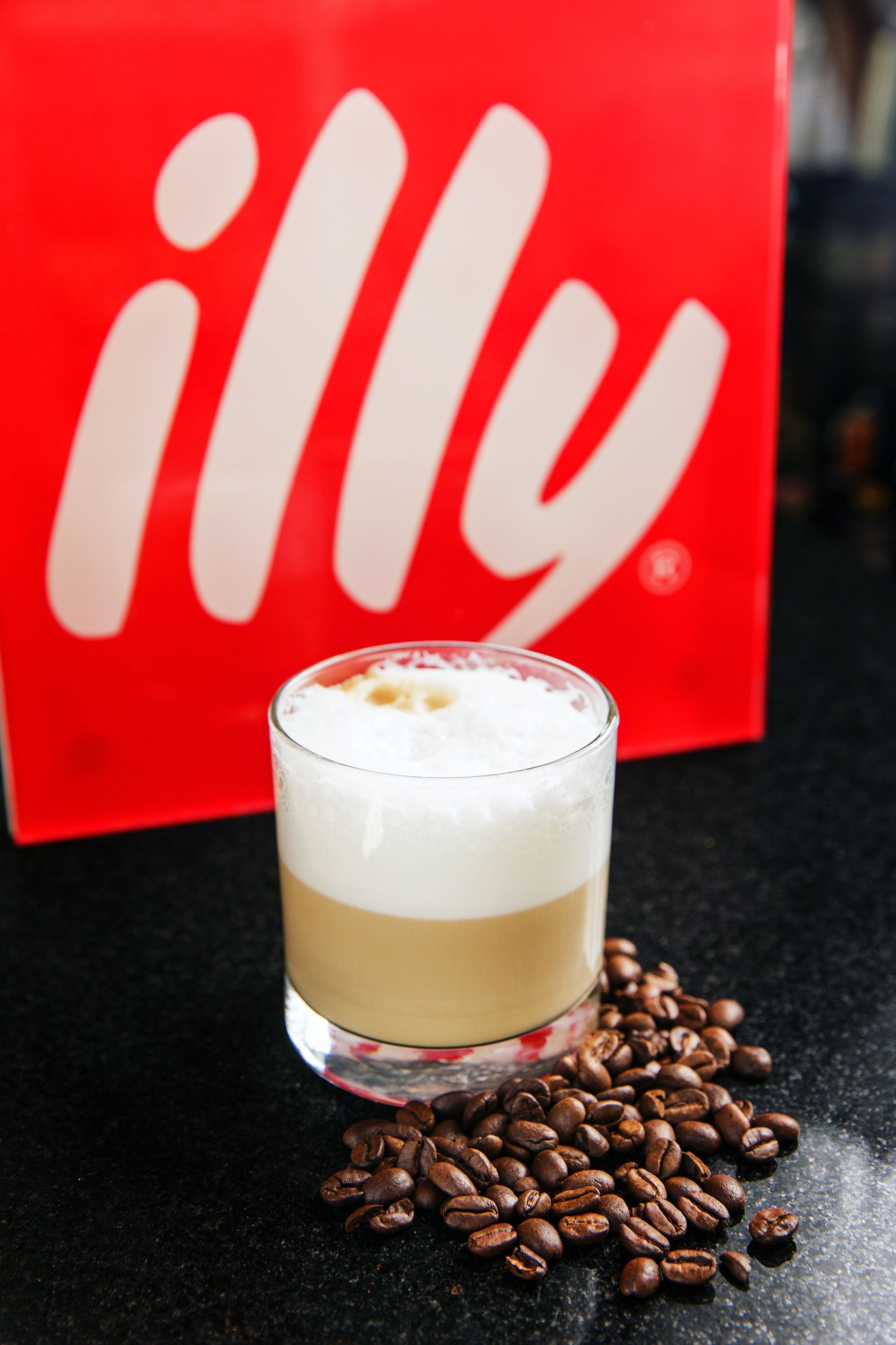 A glass of layered beverage with coffee beans scattered around it.