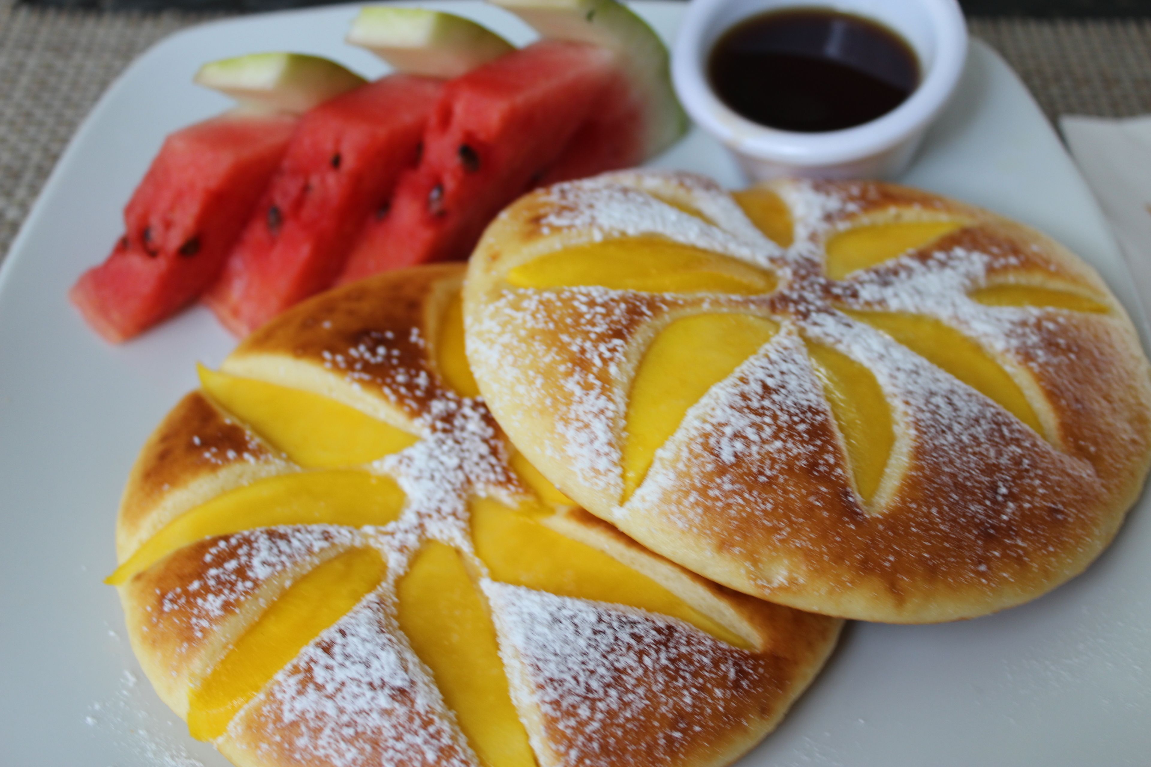 Un plato con dos pasteles cubiertos de fruta, una rebanada de sandía y un tazón pequeño de almíbar.