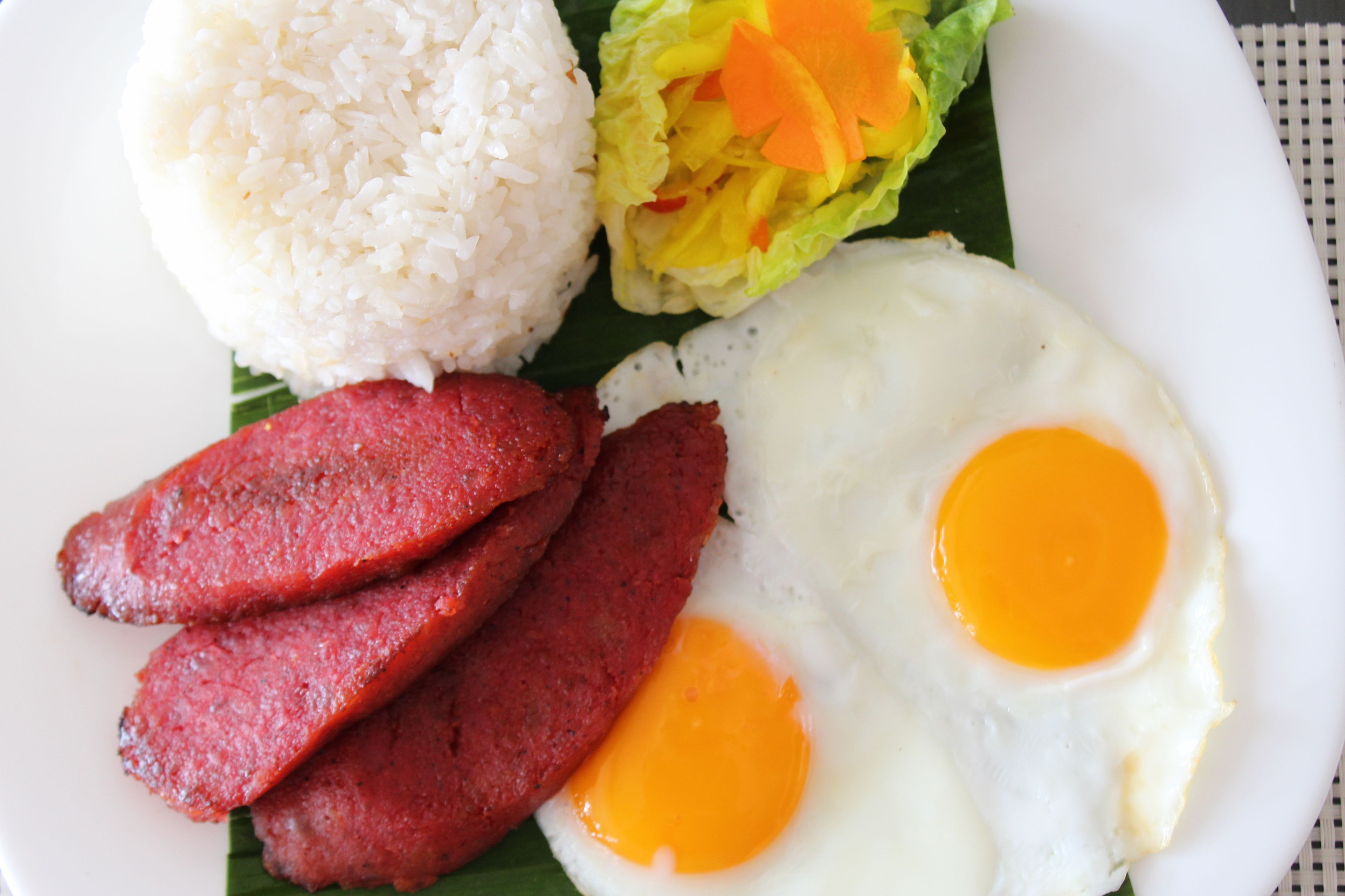 A plate with white rice, two fried eggs, and slices of red meat.