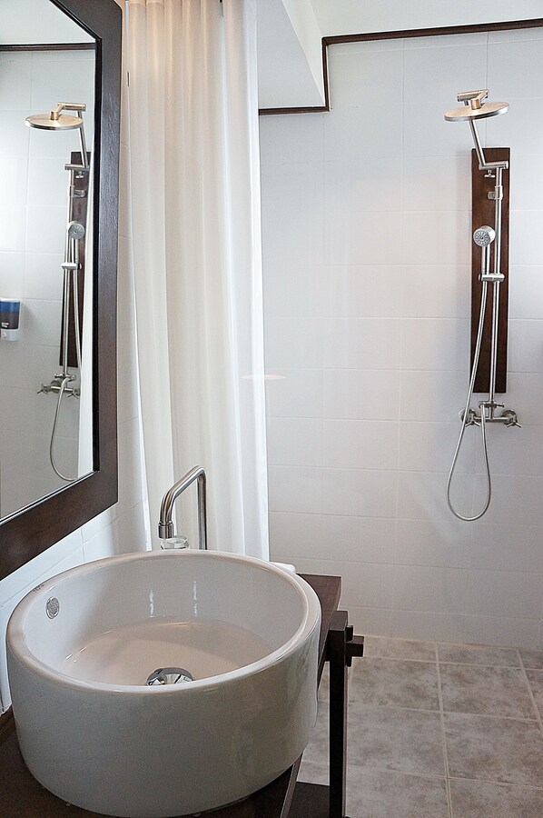 Un baño con un lavamanos grande y redondo, un espejo y dos cabezales de ducha.