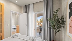 A hotel room with a bed, a potted plant, and a view of the outdoor seating area.