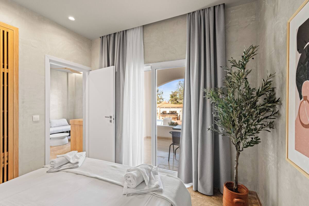 A hotel room with a bed, a potted plant, and a view of the outdoor seating area.