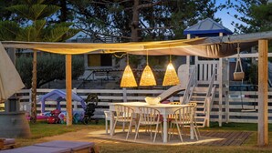 An outdoor patio area with a table and chairs, a covered seating area, and a white fence.