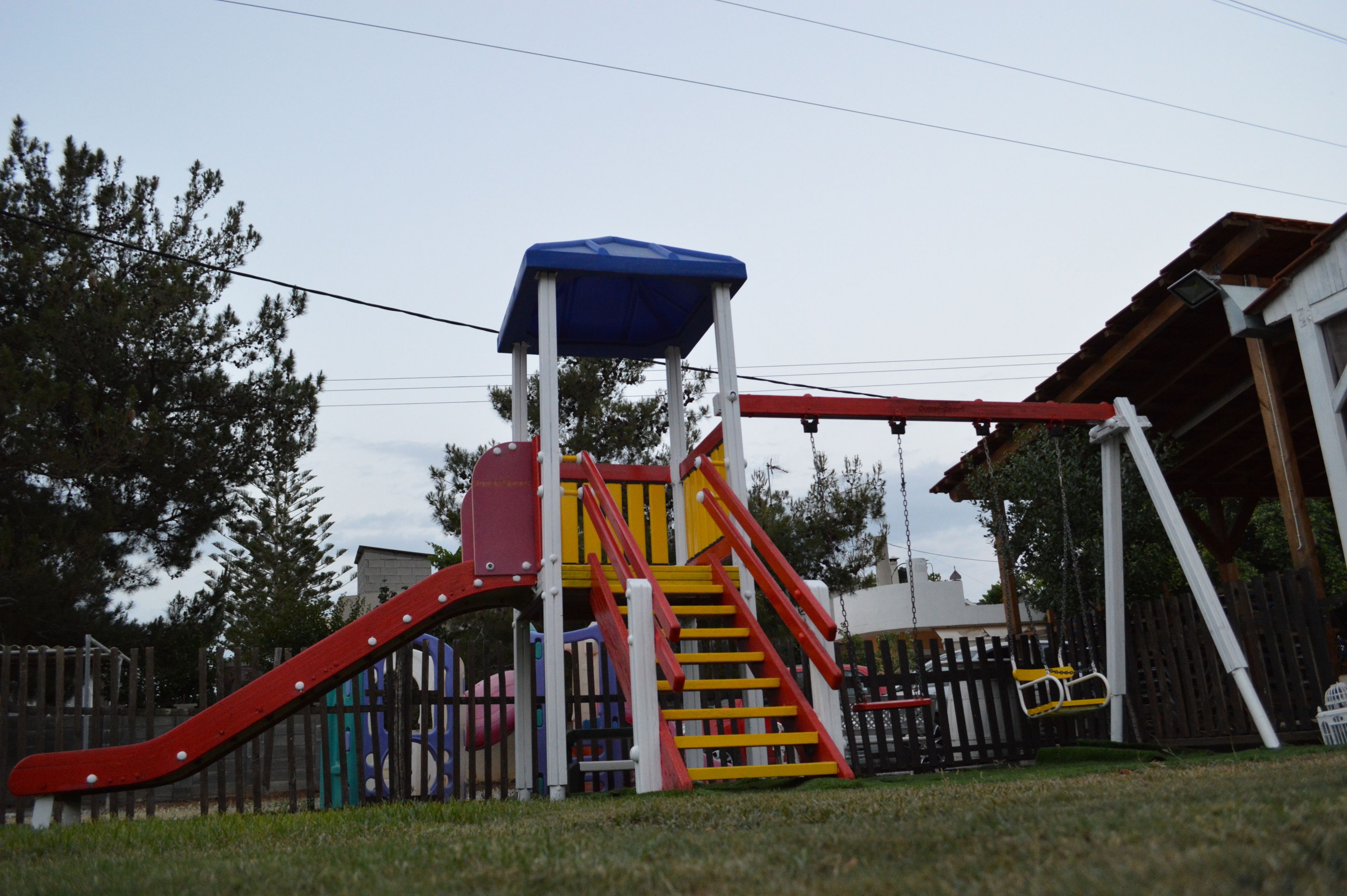 A playground with a red slide, yellow stairs, and a blue canopy.