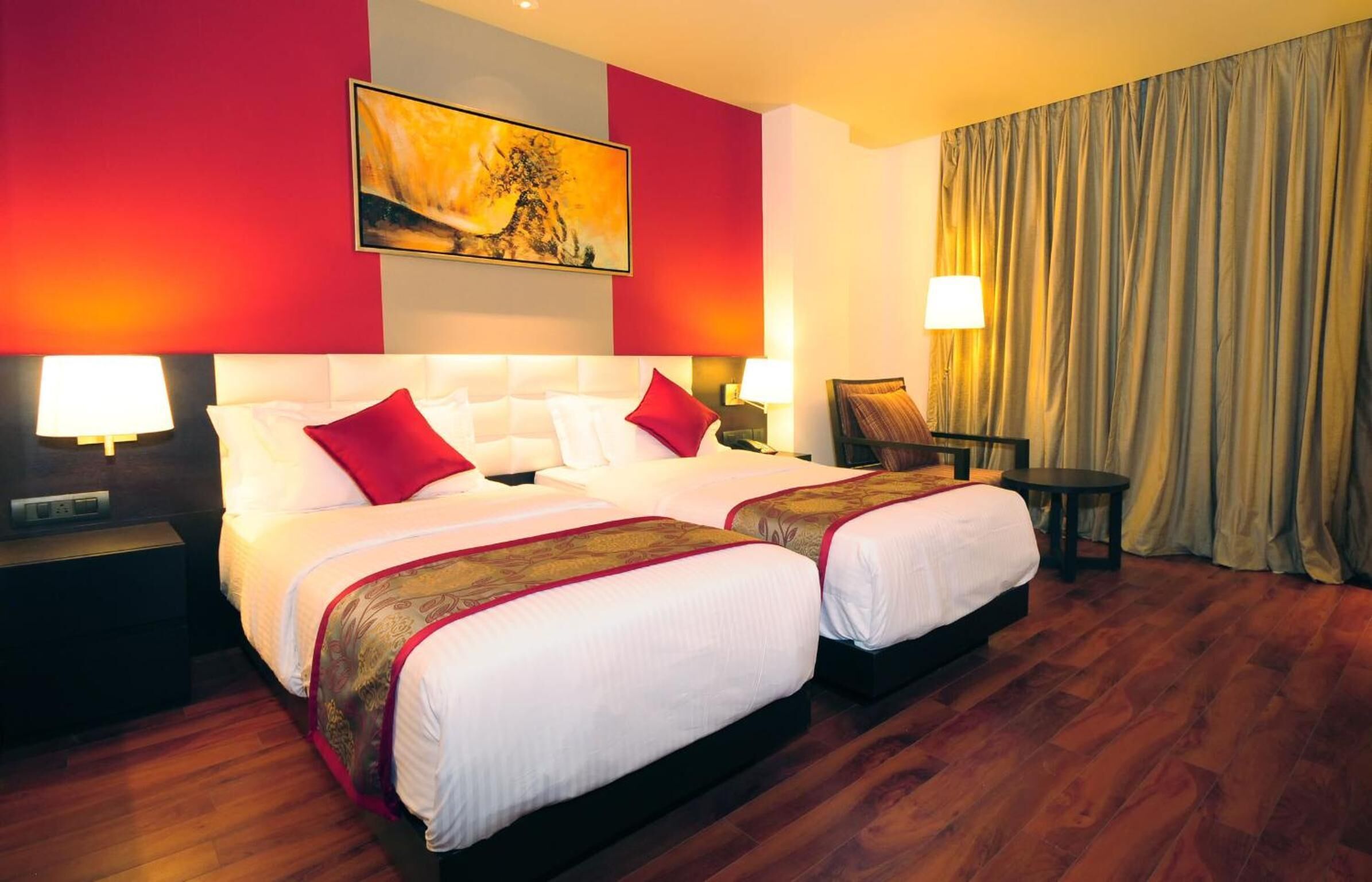 A hotel room with two beds, a large painting on the wall, a chair, and a curtain.