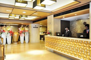 A hotel reception area with a modern design, featuring a reception desk, a large vase with flowers, and a sign that reads "hi-brew". - Senses Hotel (Barasat)