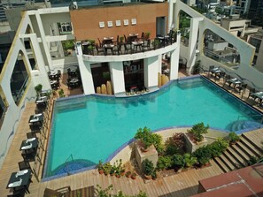 A rooftop pool with multiple seating areas and a bar. - Senses Hotel (Barasat)