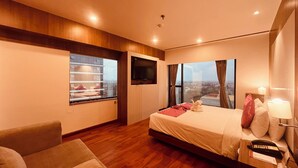 Habitació d'hotel moderna amb un llit gran, televisió, sofà i vista a la ciutat.