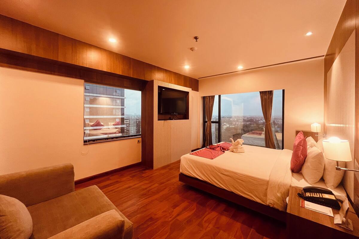 A modern hotel room with a large bed, a TV, a sofa, and a city view.