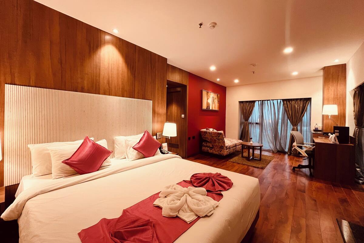 A hotel room with a large bed, a desk, a chair, and a sofa.